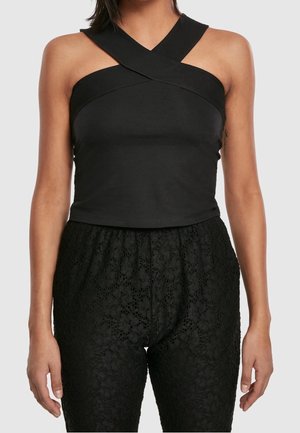 Woman wearing a black sleeveless top with crisscross straps and high-waisted black lace pants.