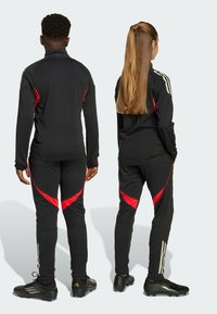 Tute sportivi neri con dettagli rossi, maglie a maniche lunghe, pantaloni attillati con dettagli laterali a contrasto e tre strisce sulle maniche.