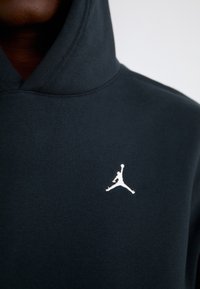 Gros plan d'une personne portant un sweat à capuche noir avec un logo Jumpman blanc sur la poitrine.
