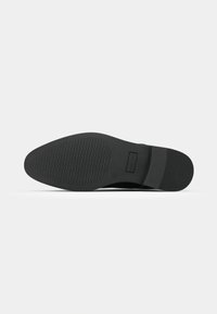 Semelle de chaussure de ville noire avec motif de traction texturé sur l’avant-pied et le talon, section médiane lisse, photographiée sur fond blanc.