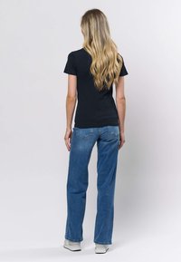 Musta ribbineuloksinen lyhythihainen yläosa yhdistettynä vaaleansinisiin suoralahkeisiin farkkuihin ja valkoisiin lenkkareihin, kuvattuna takaapäin, näkyvissä pitkät aaltoilevat hiukset.