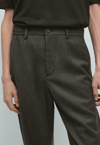 Pantaloni grigi in misto lana con vestibilità rilassata, dotati di vita elastica, chiusura con bottone e tasche laterali. Tessuto liscio e strutturato.