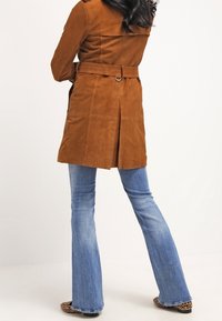 Brązowy zamszowy płaszcz trench z paskiem w talii, tylnym rozcięciem i długimi rękawami. Połączony z jasnoniebieskimi dzwonami i butami w zwierzęcy wzór.