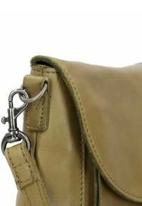 Ingrandimento dell'angolo di una borsa in pelle beige che mostra il fermaglio in metallo argentato e il punto di attacco della tracolla, con cuciture visibili e superficie texture.