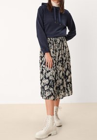 Marinblå huva sweatshirt med dragsko som matchas med en veckad midi-kjol i blommönster i svart och kräm, kompletterad med vita snörade ankelstövlar.