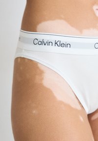 Vita bomulls-bikini underkläder med en svart Calvin Klein-logotyp på en grå midjeband, med en slät textur och högskuren bendesign.
