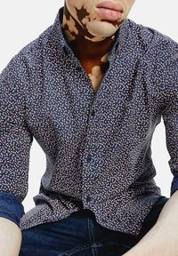 Camicia navy a bottoni con un motivo a foglie multicolore. Presenta un colletto a punta e polsini blu scuro a contrasto. Tessuto in cotone.