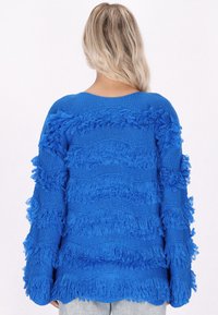 Blauer Strickpullover mit strukturierten Fransen-Details, langen Ärmeln und lockerer Passform. Glatte Stoffoberfläche mit gewelltem Muster.