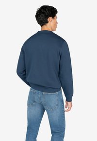 Sudadera azul marino con cuello redondeado y puños acanalados, combinada con jeans de denim azul claro que tienen dos bolsillos traseros.