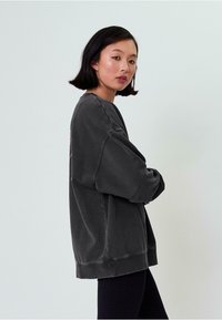 Übergroßer grauer Sweatshirt mit strukturierter Oberfläche, Drop-Shoulder-Design und geripptem Saum. Mit pinken grafischen Details auf dem Rücken.