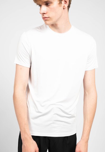 T-shirt bianco a maniche corte realizzato in morbido cotone, con collo rotondo e design aderente, esposto su uno sfondo neutro.