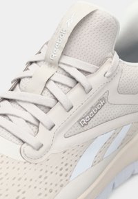 Beige sportskor med ovandel av mesh, gummisula och synligt snörningssystem. Har Reebok-logotyp och en slät läderdetalj.