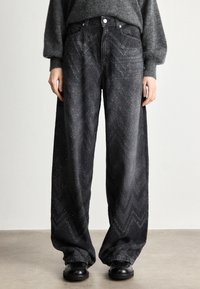 Calças de ganga largas pretas com um padrão de chevron e detalhes discretos e brilhantes. Feitas de ganga com um corte solto e cintura alta, acabadas com acessórios em metal.