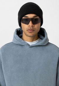 Lichtblauwe oversized hoodie met een grote capuchon, gecombineerd met een zwarte gebreide beanie en donkere zonnebril, met een casual, ontspannen pasvorm.