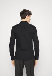Camisa negra de manga larga con cuello estándar, puños abotonados y una textura suave, que presenta un corte entallado y un dobladillo recto.