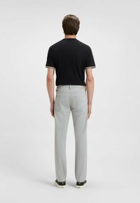 Czarna koszulka polo z białymi i beżowymi paskowanymi mankietami, zestawiona z jasnoszarymi spodniami. Model stoi tyłem, ukazując tył stroju.