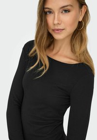 Zwarte langemouwen top met een bootnek, gemaakt van een gladde stof; de aansluitende pasvorm accentueert de lichaamsvorm, met subtiele naaddetails.
