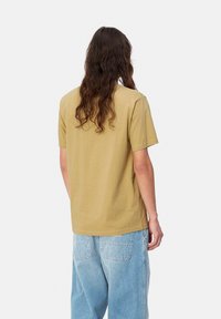 Camiseta de algodón suave de manga corta en color caqui con un corte relajado. Presenta un diseño simple y textura lisa, vista desde la parte posterior.
