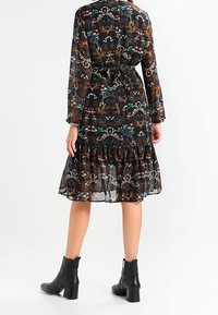 Vestito floreale nero con maniche lunghe e gonna a strati, dotato di un fiocco in vita. Indossato con stivaletti alla caviglia, che mostrano una texture trasparente.
