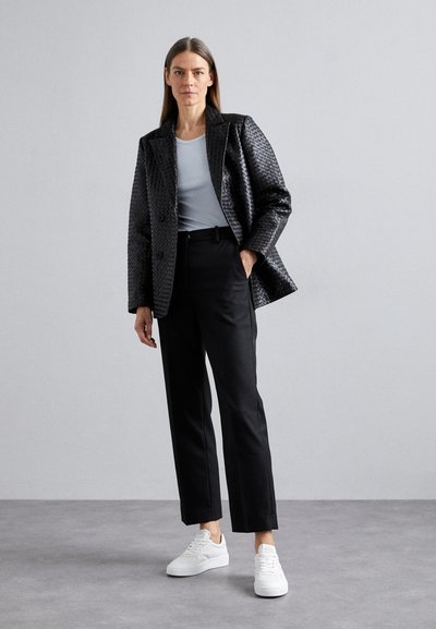 Blazer trapuntato nero con doppio bottone, camicia azzurra chiara, pantaloni neri e sneakers bianche. Design minimalista con vestibilità su misura.