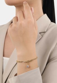 Pulsera de cadena de oro con un charm texturizado. La cadena presenta eslabones entrelazados, y el charm es redondo con una superficie brillante.