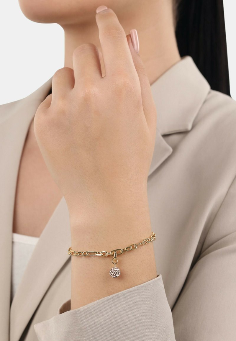 Pulsera de cadena de oro con un charm texturizado. La cadena presenta eslabones entrelazados, y el charm es redondo con una superficie brillante.