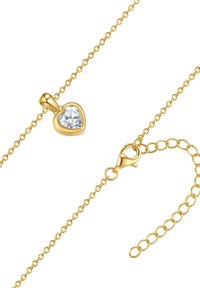 Collana d'oro con pendente a forma di cuore che presenta un gemma trasparente. La catena è texturizzata, con un moschettone e lunghezza regolabile.