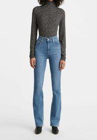 Jean bleu taille haute, coupe slim avec légère évasée, associé à un haut noir à manches longues orné d'un motif floral multicolore.