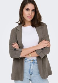 Blazer rayé gris avec deux poches avant, manches retroussées et accents à boutons, porté sur un t-shirt blanc et un jean bleu clair.