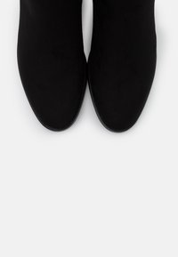 Botines negros con una textura suave similar al ante, diseño de punta afilada y una forma minimalista. Sin herrajes ni acentos visibles.