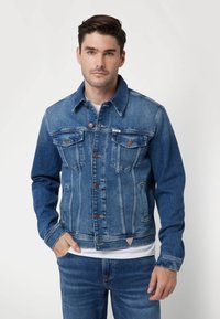 Spijkerjack in medium blauw, met een knoopsluiting aan de voorkant, twee borstzakken en contrasterende stikdetails. Regular fit, standaard kraag.