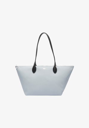 Sac fourre-tout bleu clair avec des accents et poignées en cuir noir. Présente une surface lisse et texturée ainsi qu'un détail de logo subtil à l'avant.