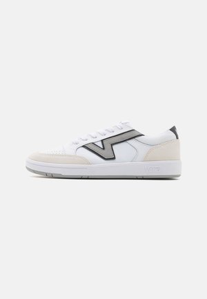 Zapatillas bajas con parte superior de cuero y textil blanco, que presentan acentos grises y una puntera de ante color marrón claro. El modelo muestra el logo de Vans.