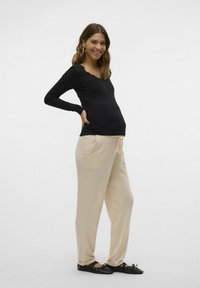 Svart ribbad långärmad topp, ljusbeige joggerbyxor med fickor och elastisk midja. Modell med svarta ballerinaskor. Enkelt bakgrund.