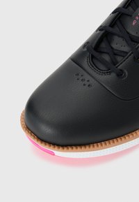 Black sneaker with a textured leather upper, featuring a rubber sole with a tan edge and pink accent. Laced design with perforated details.