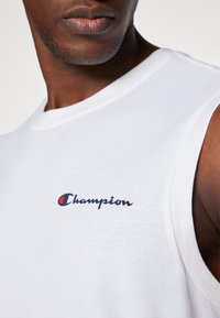 Witte mouwloze shirt van katoen met een blauwe geborduurde "Champion" logo op de borst, gladde textuur en een ronde halslijn.