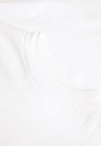 Vit bomullströja med rundad halsringning och korta ärmar, som visar subtil textur och en slät yta.