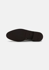 Sole di scarpa in pelle nera con texture liscia, caratterizzata da una forma appuntita e arrotondata e un logo discreto. Leggero motivo di battistrada per aderenza.