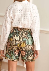 Shorts à motifs floraux dans des tons terreux avec une taille élastique, associés à une chemise blanche à boutons en dentelle avec un col.