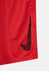 Crvene atletske kratke hlače s glatkom teksturom, s velikim crnim Nike logotipom sa strane, dizajnirane za udobnost i pokretljivost.