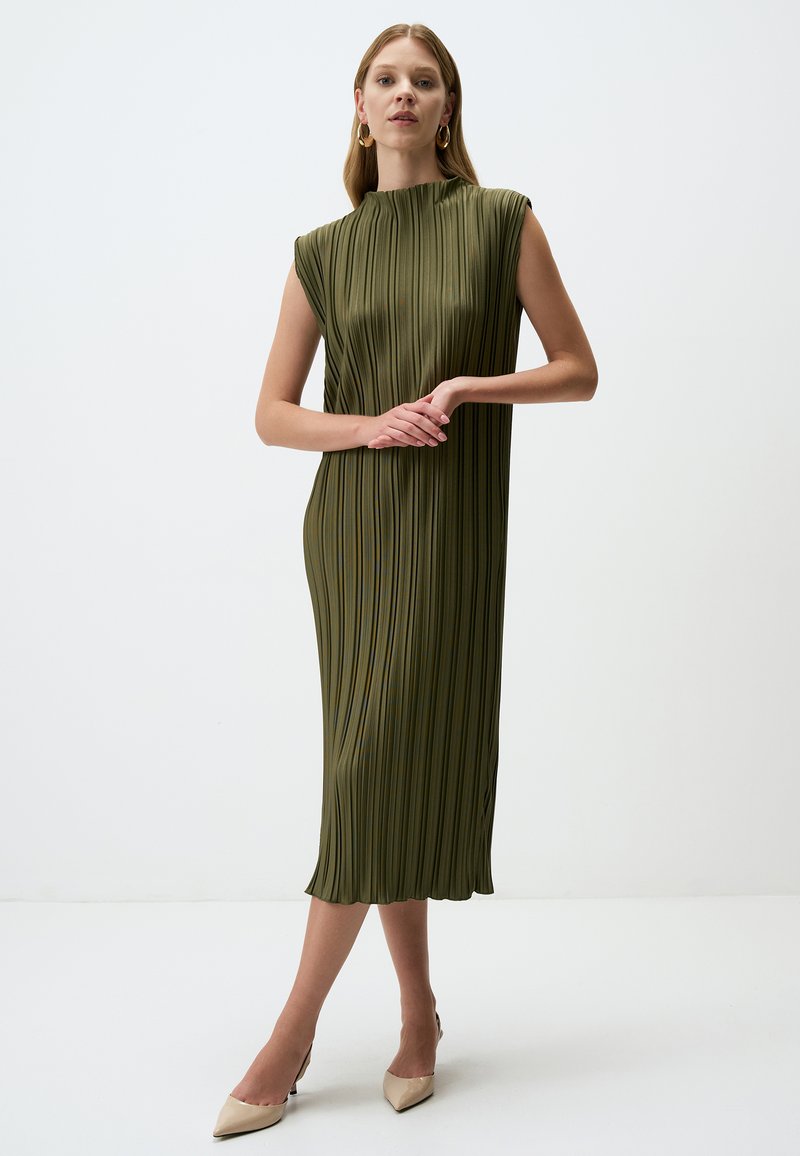 Olivgrünes Midi-Kleid mit vertikalen Falten, hohem Hals und Kurzärmeln. Glatte Textur mit einem dezenten Glanz. Getragen mit beigen Absätzen.