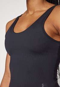 Sort atletisk tanktop lavet af glat, strækbart stof. Har en scoop halsudskæring og en tætsiddende design. Diskret logo-detalje på siden.