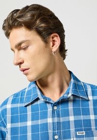 Blauw-wit geruite Wrangler-shirt met een klassieke kraag, knoopsluiting en een klein logotag aan de linkerkant. Zachte stoftextuur.