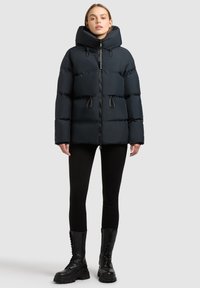 Black puffer jacket with a high collar, drawstring details, front zipper, and quilted sections, paired with black leggings and combat boots.