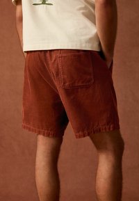 Shorts en velours côtelé marron avec une poche arrière et une coupe décontractée. La texture est nervurée, avec un ourlet qui se termine juste au-dessus du genou.