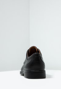 Scarpa in pelle nera con punta arrotondata, texture liscia e interno marrone a contrasto. Presenta dettagli di cucitura discreti e una suola in gomma bassa.