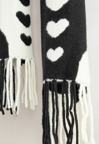 Écharpe noir et blanc en matériau doux, avec des motifs de cœurs alternés et des bords frangés, présentant une finition texturée.