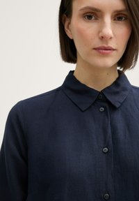 Cămașă bleumarin dintr-un material moale și texturat, cu un guler clasic și închidere cu nasturi pe față. Design simplu, fără modele sau accente.