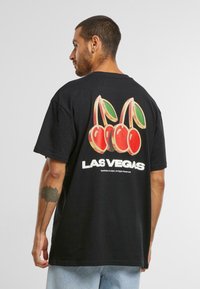 Sort bomuld t-shirt med korte ærmer. Har et farverigt kirsebærtryk og "LAS VEGAS" tekst trykt på ryggen.