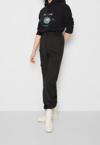 Černé cargo kalhoty s vysokým pasem, vybavené bočními kapsami a elastickými manžetami, párované s černou mikinou a bílými gumovými botami.